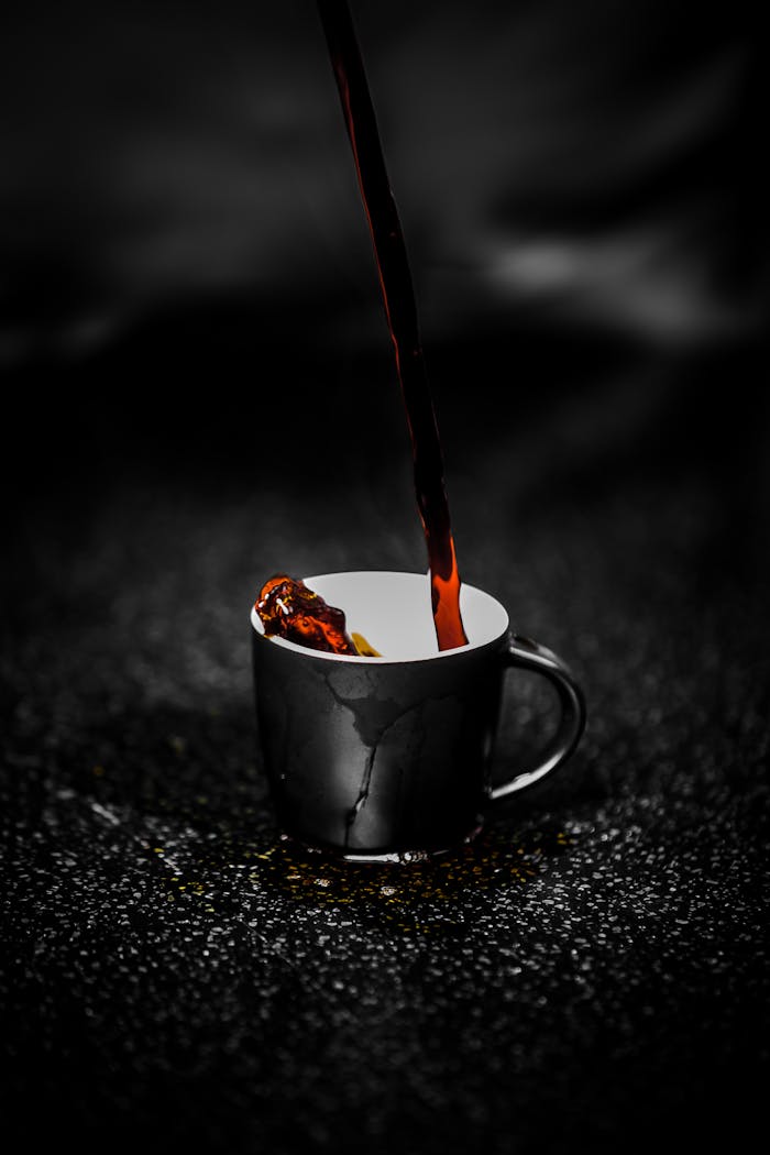 Close-up of steaming dark coffee being poured into a black cup on a dark textured surface. Rich aroma.